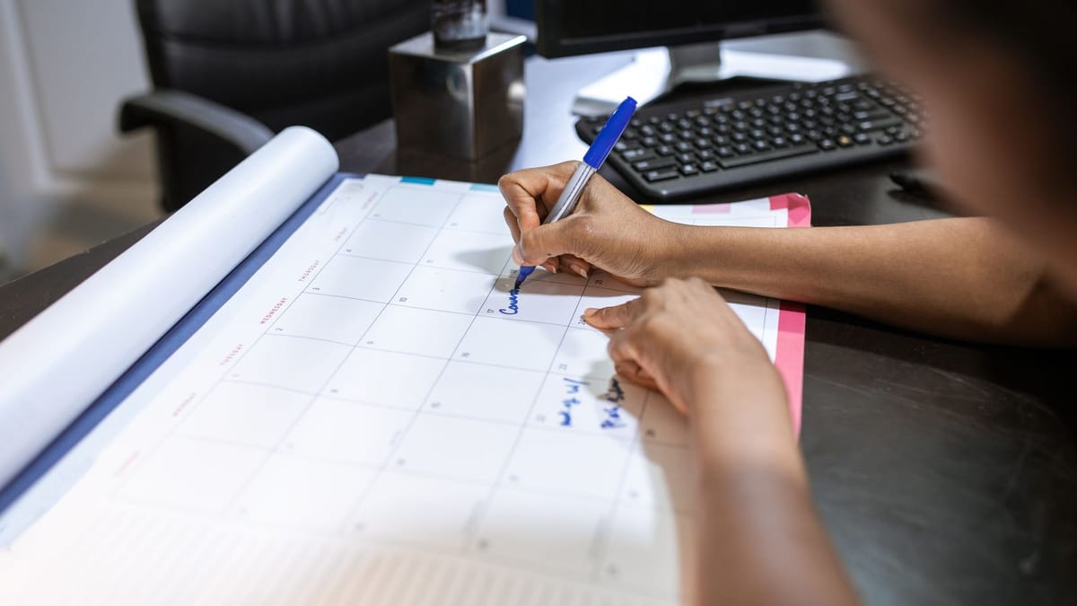 Woman marking dates on a monthly desk calendar