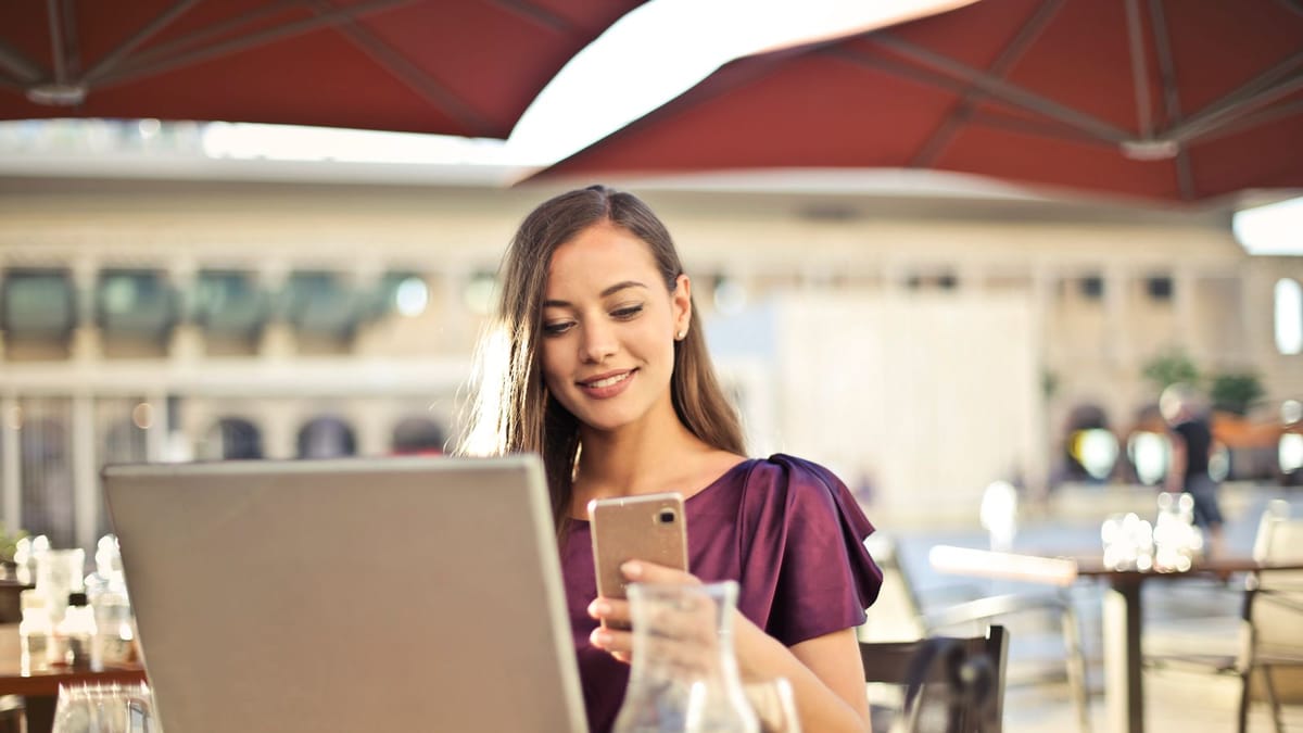 Young creator checking her phone and laptop at a café