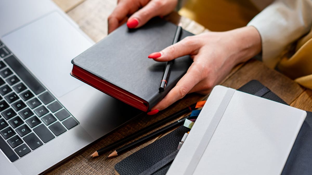 Woman's hands with red nails organising notebooks next to a laptop