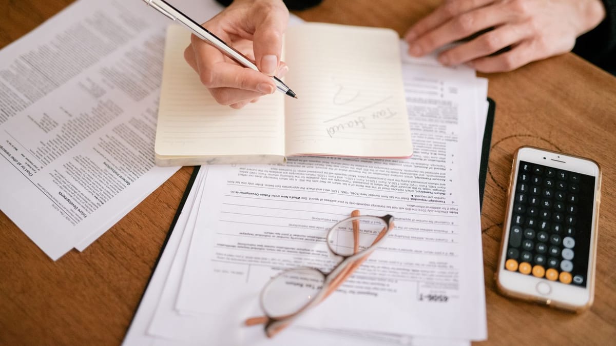 Woman's hands taking notes next to tax forms and a calculator